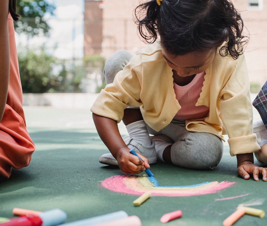 A child drawing a rainbow with chalk outdoors